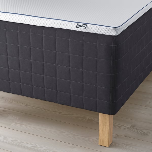 Close-up of ikea mattress on dark base with wooden legs.