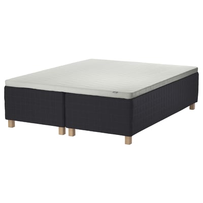 Black wooden base bed with white mattress, four wooden legs, grid-patterned fabric.