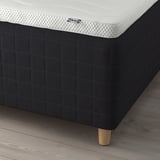 A modern bed setup with a black frame. It includes a white mattress with pocket springs for support and comfort. The frame has wooden legs.