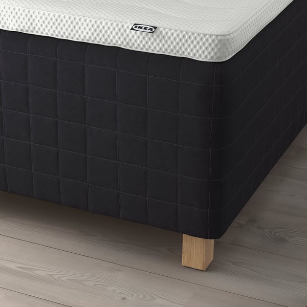 Close-up of a white IKEA mattress on a black bed frame with wooden legs.
