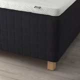 Close-up of a white IKEA mattress on a black bed frame with wooden legs.