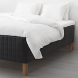 Modern bed with black quilted wooden-base mattress, white sheets, and wooden legs.