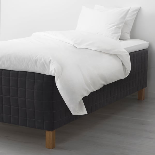Modern bed with black headboard, white linens, wooden legs, sprung mattress.
