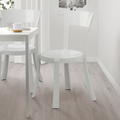 Two white STEIN stackable chairs near a small table. Lightweight, durable plastic, ideal for compact dining.