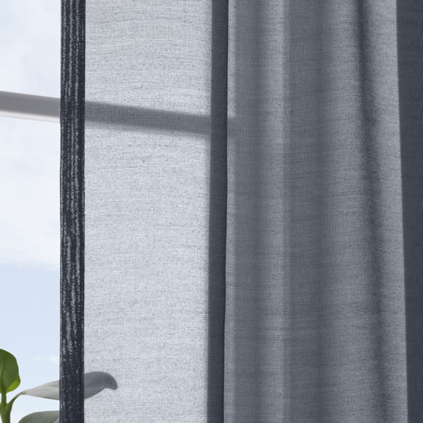 Dark blue sheer curtains hang near a window, softening sunlight and providing privacy. A green leaf is visible at the bottom left.