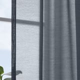 Dark blue sheer curtains hang near a window, softening sunlight and providing privacy. A green leaf is visible at the bottom left.