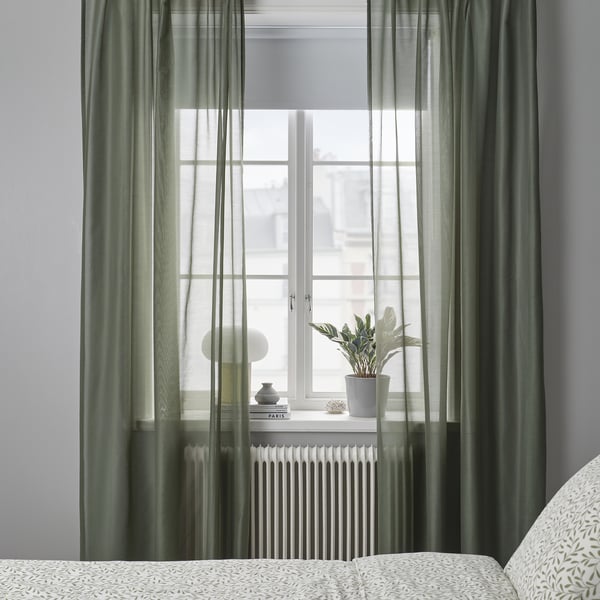 Green STENFRÖ curtains filter sunlight beside a window, adding calm. Plant and decor on sill, curtains below.