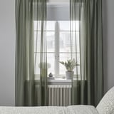 Green STENFRÖ curtains filter sunlight beside a window, adding calm. Plant and decor on sill, curtains below.