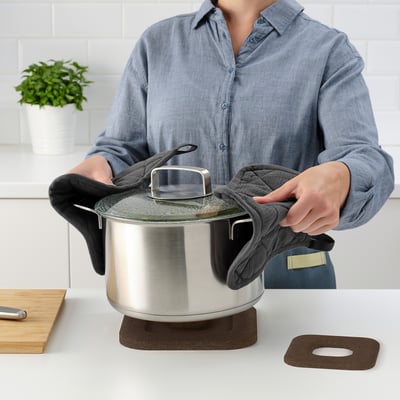 A person uses a STENPOTT trivet to lift a pots lid on a countertop.