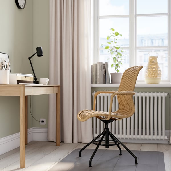 Minimalist home office with light wood desk, black adjustable STIGBYGEL chair, white radiator, potted plant & books on window sill.