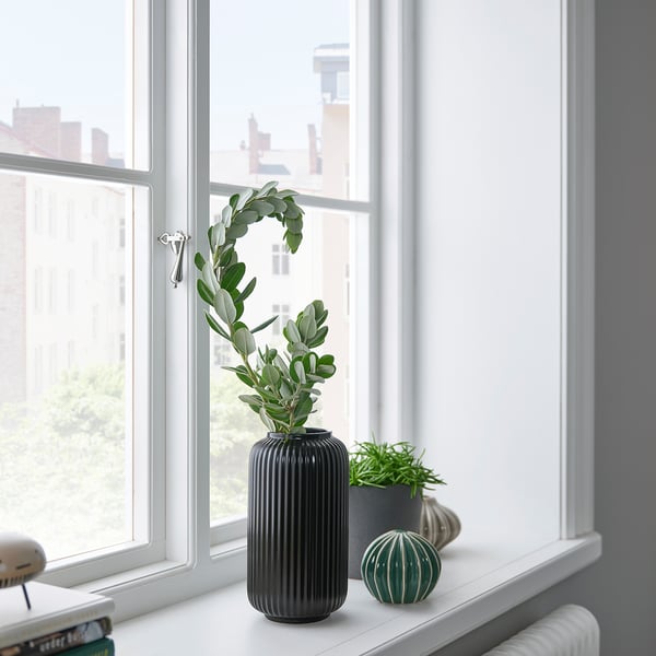 Black ribbed STILREN vase with green foliage on windowsill.