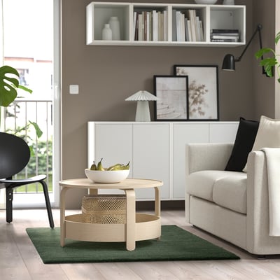 Modern living room with grey sofa, wooden table, green rug, black chair, white cabinet, bookshelf, black lamp, large window.