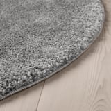 Close-up of a soft, plush round rug in light gray on a wooden floor, showcasing its dense, textured pile.