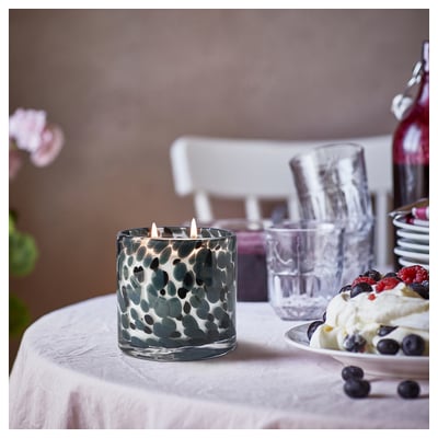 A lit blue-green patterned glass candle sits on a table with glasses and berry-topped dessert.