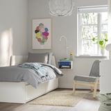 Modern bedroom with gray bedding, hanging light, art, floating STOMSÖ with blue drawer, chair, and plants.