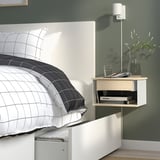 Modern bedroom with wall-mounted nightstand, featuring storage and holding lamp, glass, plants.