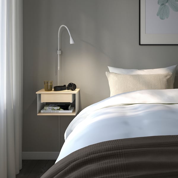 A cozy bedroom with a STOMSÖ white bedside table, blue drawer, and wall lamp.