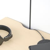 Black headphones rest on a beige surface beside a gray wall-mounted table with a cut-out for cables.