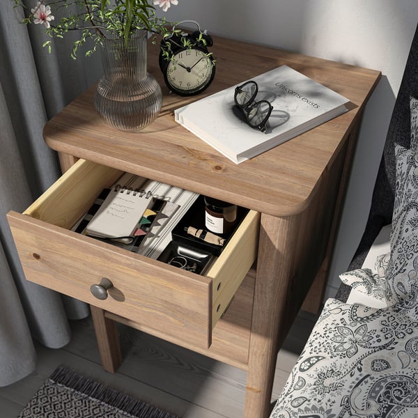 Wooden bedside table with open drawer showing items, including a book, glass, and clock on top.