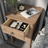 Wooden bedside table with open drawer showing items, including a book, glass, and clock on top.