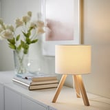 Small white STORSEGEL lamp with wooden tripod base, next to flowers and books, warm light.
