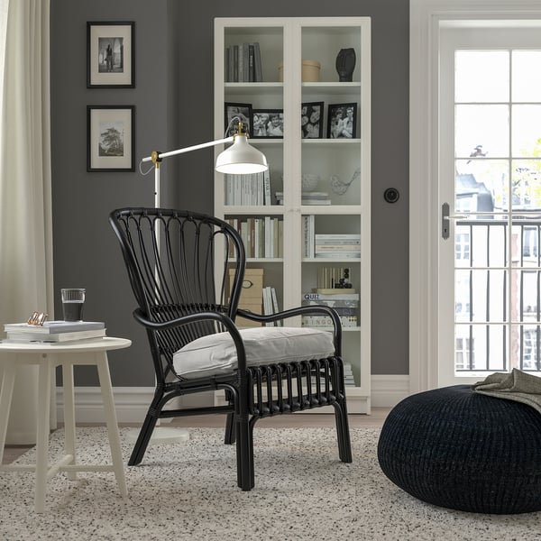 Modern living room with STORSELE black armchair, white cushion, round table, bookshelf, lamp, window, gray rug, black ottoman.