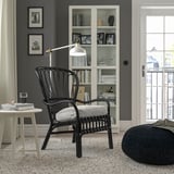 Modern living room with STORSELE black armchair, white cushion, round table, bookshelf, lamp, window, gray rug, black ottoman.