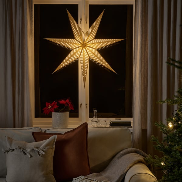 Golden star light outside window, bright night, red poinsettia, cozy couch.