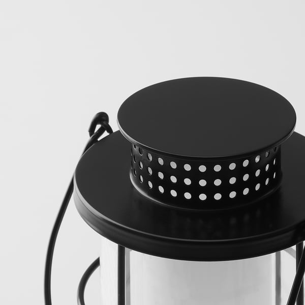 Black lantern with metal handle, featuring a perforated design for ventilation and a glass cover at the bottom, standing against a white background.