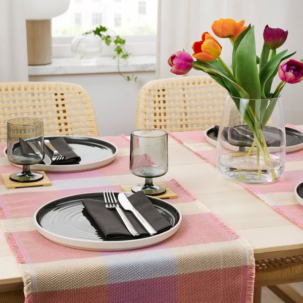Table set with STRANDFLOKA runner, plates, cutlery, glasses, and a vase with tulips.