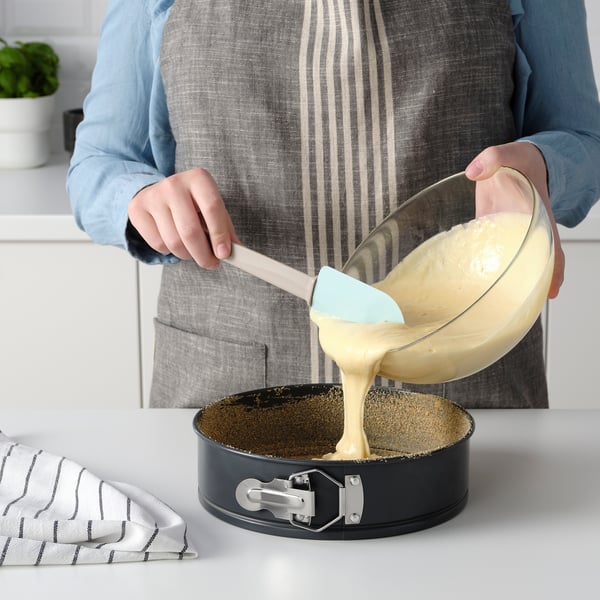Person pouring cake batter into a non-stick springform pan on a countertop.