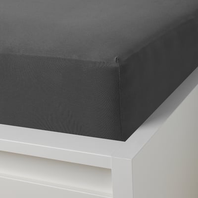 A gray fitted sheet with elastic edges on a white bed frame, designed to securely fit mattresses up to 33 cm thick.