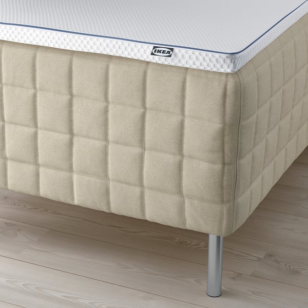 Corner of a tan mattress with visible spring legs, displaying brands and comfort.