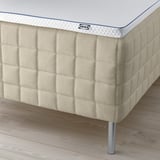 Corner of a tan mattress with visible spring legs, displaying brands and comfort.