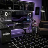 Modern gaming room with STYRSPEL black chair, purple lights, dual monitors, accessories, and a cozy couch.