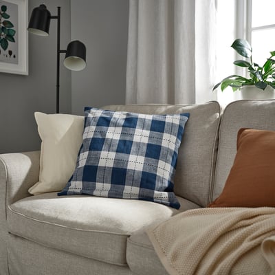 Cozy living room with light-colored couch, checkered pillow, lamp, and house plant.