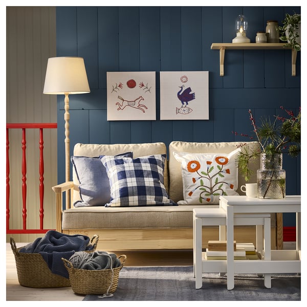 Cozy living room with blue checked cushions, dark blue wall, white table, red chair, wooden lamp, baskets, plants & wall art.