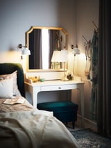 A bedroom with a gold-framed mirror, a white desk, and green cushioned stool; elegant and cozy decor.