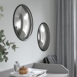 Two oval mirrors hang on a wall, reflecting light and adding depth. Below, a desk holds books and a wooden box.