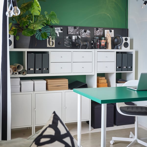 Modern green office with white storage, desk, plant, and blackboard.