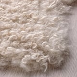 Soft, curly white rug on wooden floor; cozy, textured