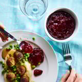 Meal with meatballs, peas, mashed potatoes, jam, spoon, fork, bowl, blue tablecloth