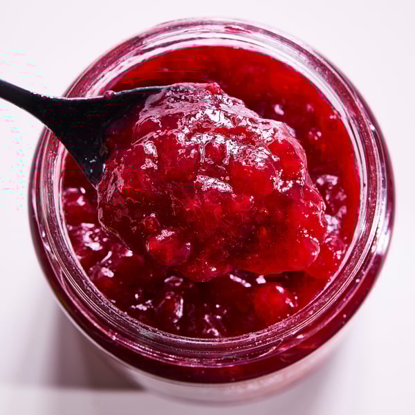 Open jar of bright red lingonberry jam, spoonful lifted, glass container.