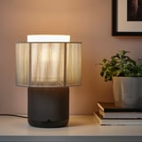 A modern lamp with a wifi speaker base sits on a table. The lamp is on, casting light, and the speaker is likely playing music.