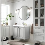 Chrome mirror reflects organized grey bathroom vanity with storage.