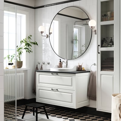 Modern bathroom with TÄNNFORSEN white vanity, round mirror, black checkered floor, and potted plant.