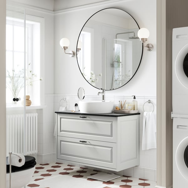 A modern bathroom with a TÄNNFORSEN light grey vanity. It has a round basin and drawers, with spherical sconces and hexagonal floor tiles.