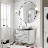 A modern bathroom with a TÄNNFORSEN light grey vanity. It has a round basin and drawers, with spherical sconces and hexagonal floor tiles.