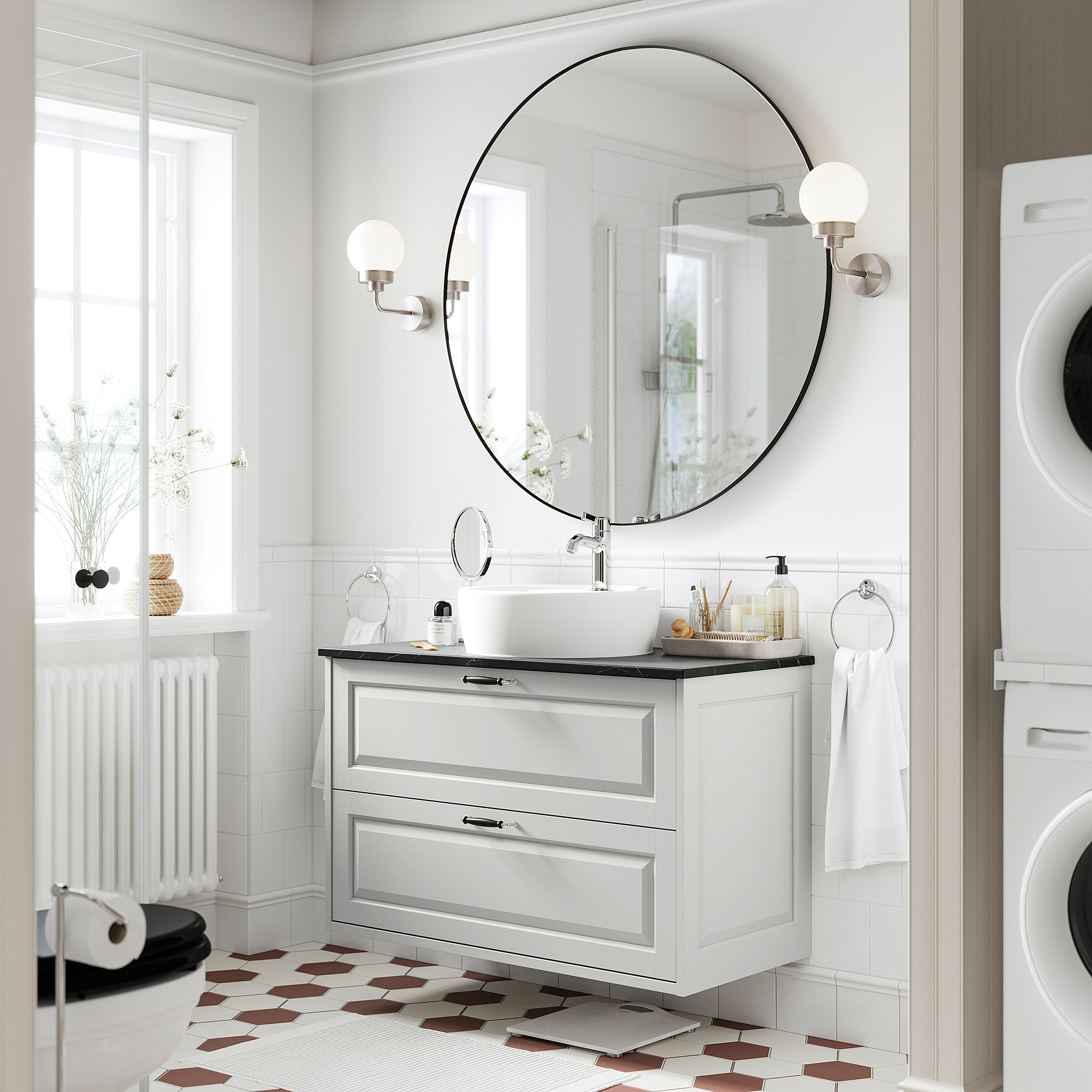 A modern bathroom with a TÄNNFORSEN light grey vanity. It has a round basin and drawers, with spherical sconces and hexagonal floor tiles.