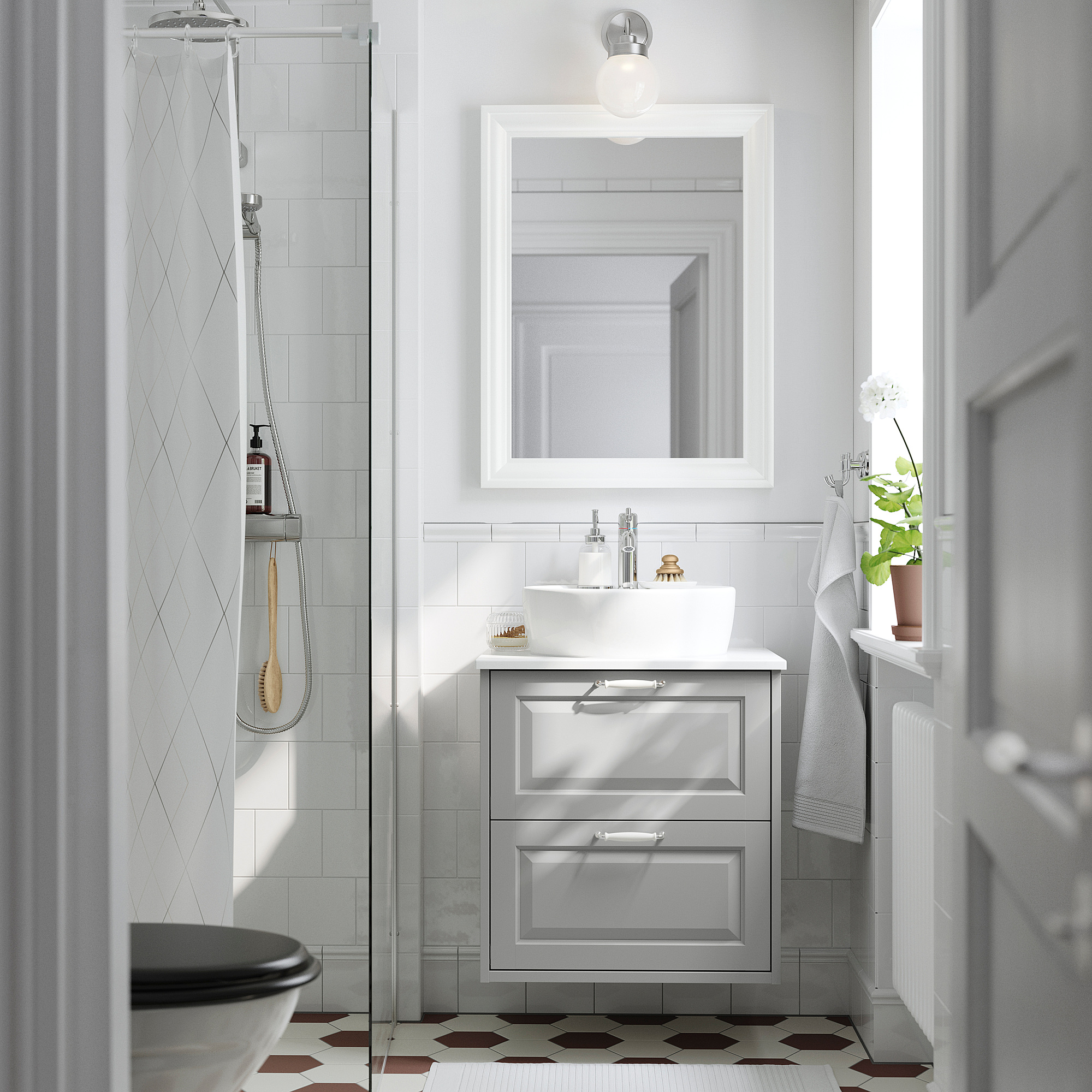 Modern bathroom with white TÄNNFORSEN vanity, vessel sink, wall-mounted mirror, glass shower, patterned tiles, and potted plant.